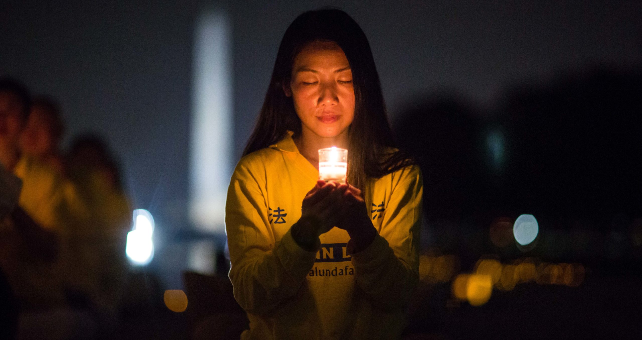 A woman joins Falun Gong practitioners holding a candlelight vigil at the Lincoln Memorial in Washington D.C.