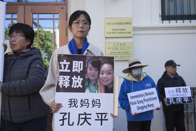 Ms. Liu Zhitong holding a board featuring a photo with her mother. The board reads, “Immediately release my mother Kong Qingping.”