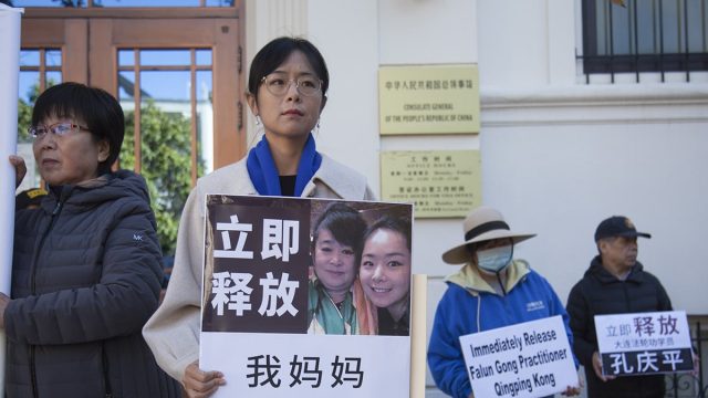 Ms. Liu Zhitong holding a board featuring a photo with her mother. The board reads, “Immediately release my mother Kong Qingping.”