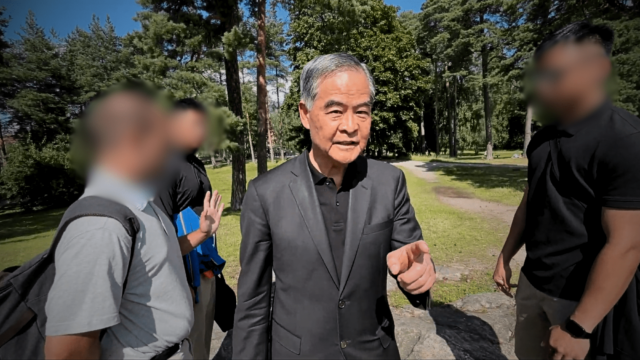 Leung Chun-ying (center) approaches and verbally confronts a Falun Gong practitioner in a public park in Finland.
