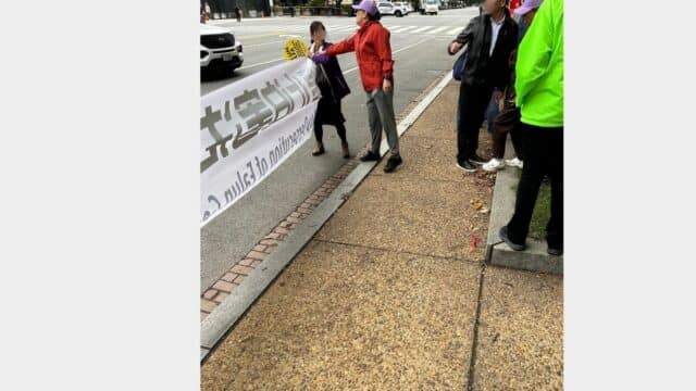 1:14:03 p.m.—the woman in the red jacket extends her right arm toward the practitioner, who is holding the banner and the yellow sign. This is the moment both eyewitnesses describe as an attempt to seize the banner.(ZXH)